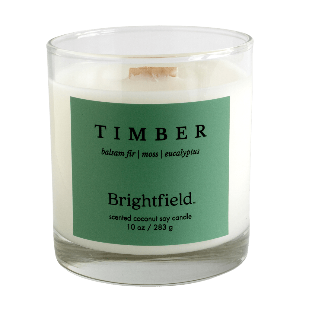 10 oz glass candle with a green label that says Timber. The scent is Timber, a woodsy blend of balsam fir, moss and eucalyptus. Made by Brightfield, a candle company in Toronto.