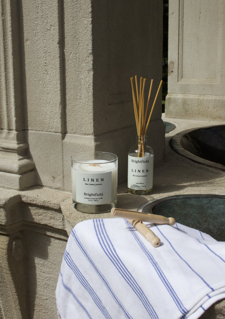 A wood wick candle sits beside a natural reed diffuser, both made in Canada by Brightfield, a Toronto candle shop